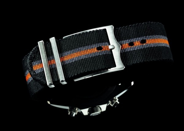 Tudor Heritage Chrono的黑色、灰色及橙色條紋的織物錶帶，搭配了參考車座的仿古安全扣。