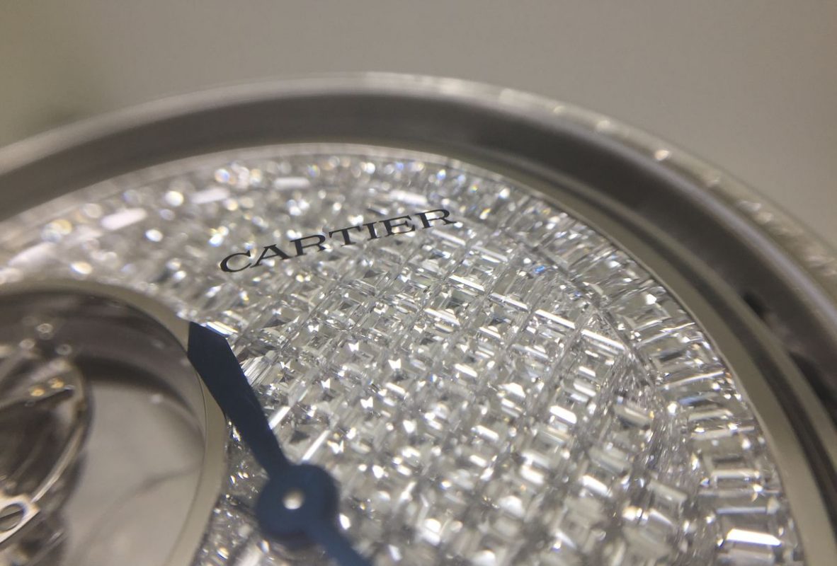 全新的Rotonde de Cartier三問報時雙重神秘陀飛輪腕錶於面盤上鑲嵌了緊密的切割鑽石。「Cartier」品牌字樣則印於藍寶石水晶鏡面內。