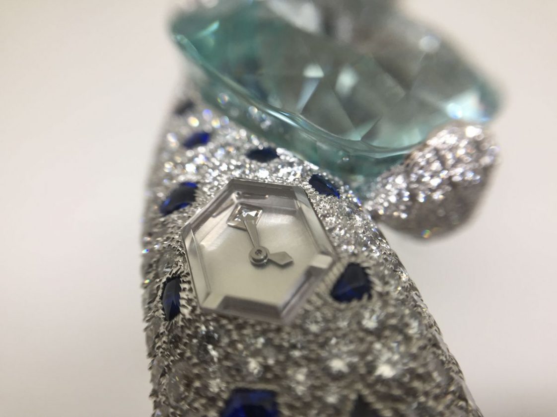 海水藍寶石下方呈現精緻的六角形錶盤，搭配鑲嵌於周圍的鑽石、藍寶石，十分華麗。