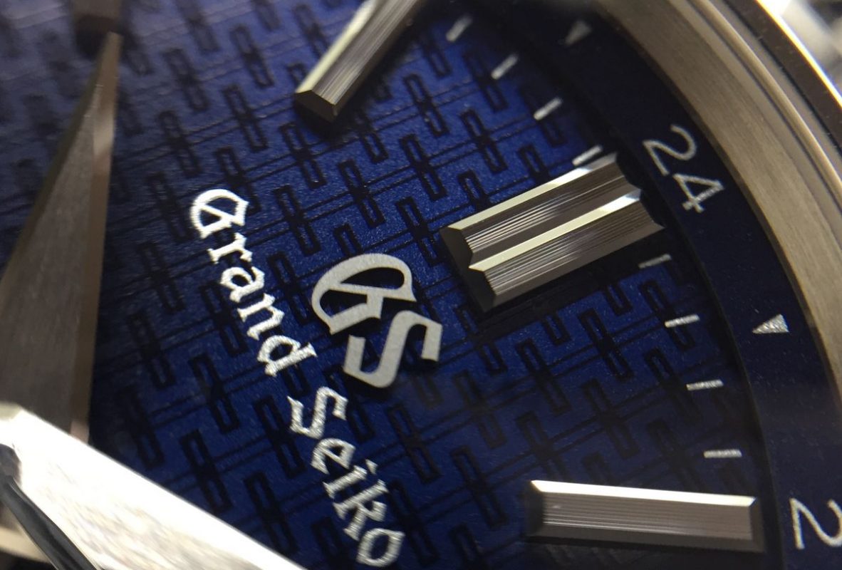 藍色錶盤上印有絣織技法般的縱橫線條，時標上方則以細微的線條修飾。